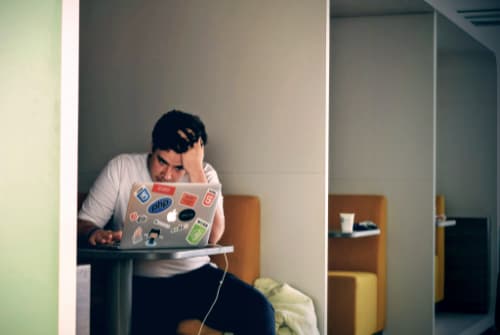 Photo of a student looking stressed while working on a laptop